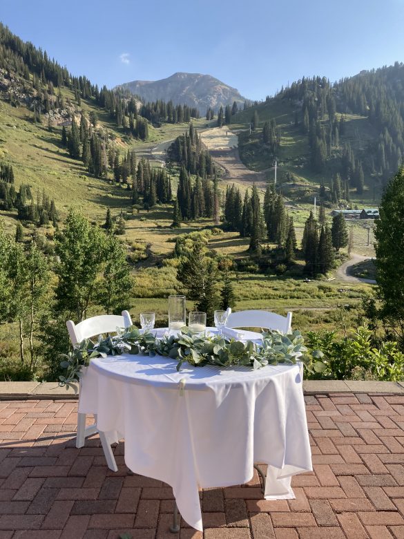 table set for two with white linens, greenery garland, mount baldy and alta ski area in background